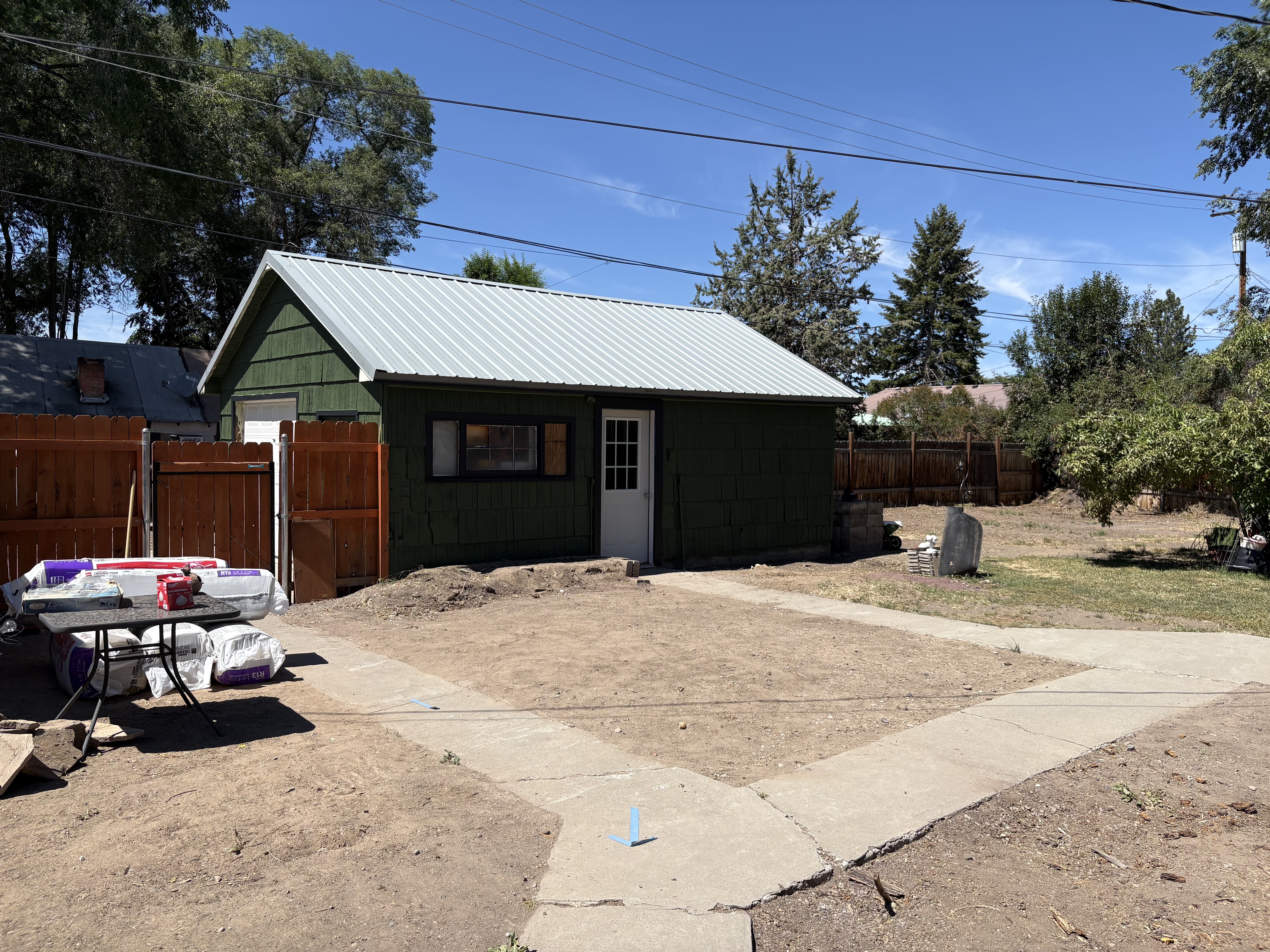 Green outbuilding before remodel – dirt yard and metal roof